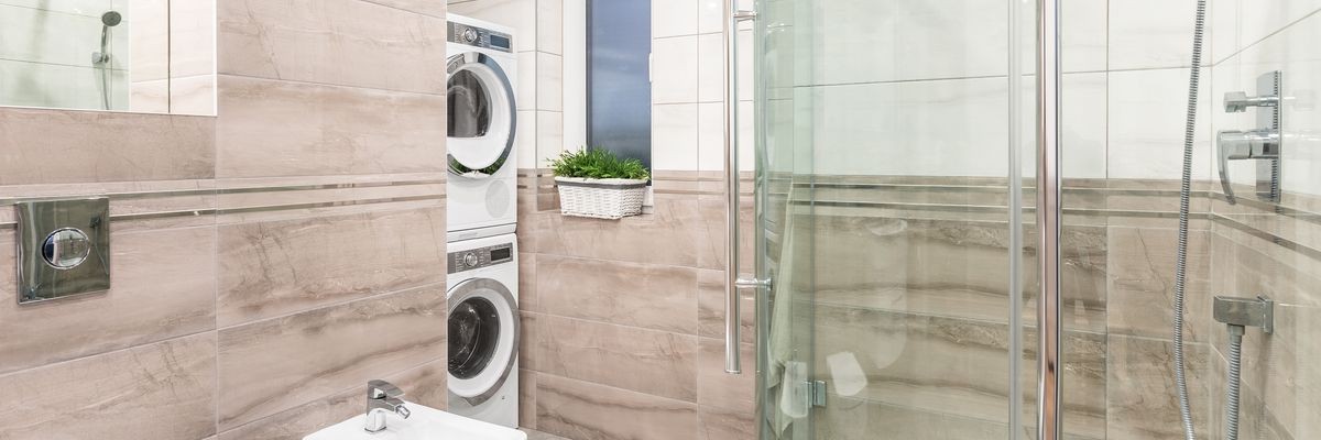 Panoramic photo of elegant bathroom with big shower, washing machine and clothes dryer